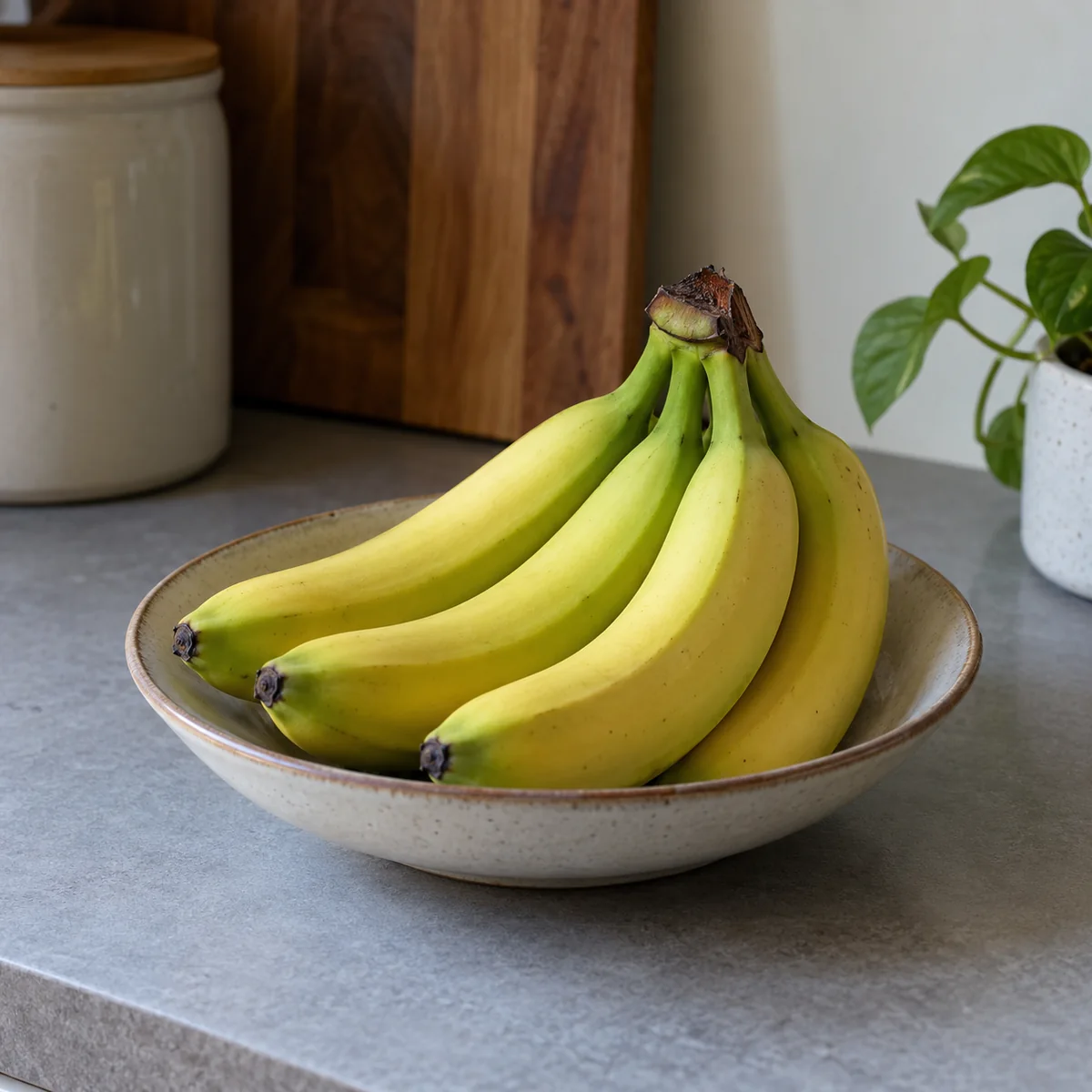 Green-tipped bananas in an open shallow bowl on a kitchen counter away from heat